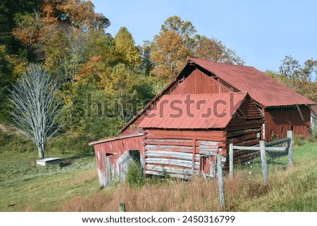 Red, wooden log barn sit on the side of a hill in Tennessee.  Paint has faded and weathered.  Rustic fence runs in front of barn.
