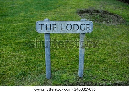 The lodge text on metal street house home sign post metal bars beams stuck into the ground grassy yard dirt black font carved in round circle of earth old tree UK residential area lawn mown