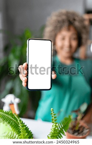 Mature mixed race smiling woman gardener working in home garden, using mobile phone app to determine what is wrong with a plant