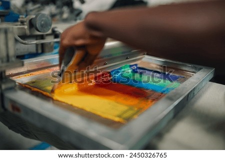 Close up of multicultural graphic technician's hands using rubber blade on silk screen frame at printing workshop. Cropped picture of african american worker's hands using squeegee for screen printing