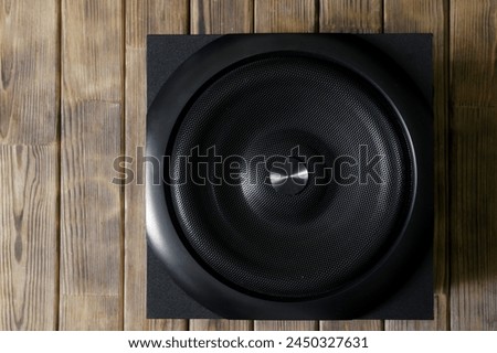 Large and powerful cubic subwoofer in a wooden enclosure with metal grille on a background of natural pine boards. Audiophile concept. Natural style. Vertical stripes. Close-up Royalty-Free Stock Photo #2450327631