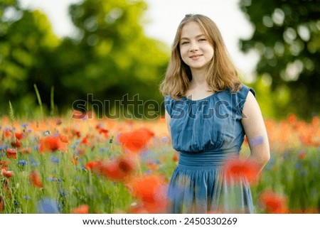 Beautiful teenage girl admiring poppy and knapweed flowers in blossoming poppy field on sunny summer day. Beautiful summer scenery near Vilnius, Lithuania.