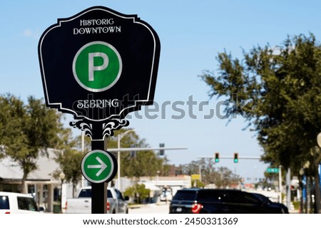 Parking sign in the Sebring Historic Downtown afrea.
sign in black with a green circle and white P. There is a light blue sky in background, as well as out of focus street, cars,  and trees