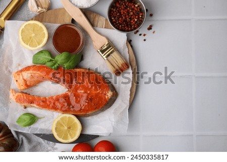 Fresh marinade, fish, lemon, brush and basil on white tiled table, flat lay. Space for text