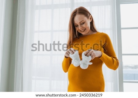 Pregnancy motherhood people expectation future. Pregnant woman with big belly holding newborn baby booties smiling at home. Young mom enjoying pregnancy. Maternity tenderness parenthood new life Royalty-Free Stock Photo #2450336219