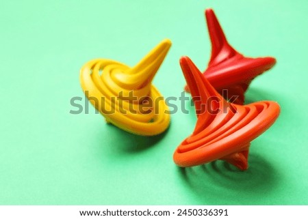 Many colorful spinning tops on green background, closeup. Space for text Royalty-Free Stock Photo #2450336391