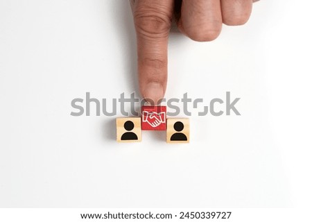 Hand puts a wooden cube with handshake agreement icon symbol between two person icon cubes, concept of business agreement, deal, partnership or cooperation between parties.
