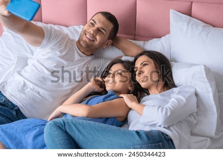 Happy young man father husband taking selfie with his wife woman daughter child kid. Caucasian family lying on bed spending time weekend and taking selfie at home