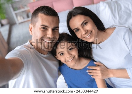 Top view shot of happy young man father husband taking selfie with his daughter child kid woman wife mother. Family standing in bedroom and taking selfie at home.