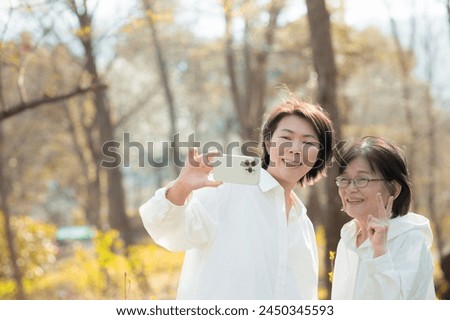 Japanese parent-child selfie of an elderly mother and child taking a picture together on camera after a leisure or outing to an outdoor park. Autumn and winter images.
