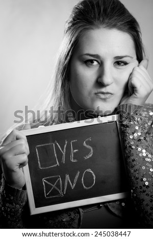Black and white portrait of angry woman holding blackboard with negative answer checked