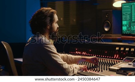 Control room sound engineer editing music with sliders and knobs, working on post production in professional soundproof studio. Technician producing songs on stereo mixing console. Camera A.