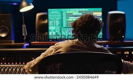 Music producer finishing a track with audio software and mixing console in control room, working with technical equipment in professional studio to process sounds. Audio technician at work. Camera A.