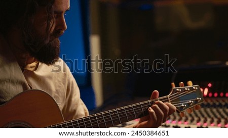 Skilled artist singing on his guitar and recording tunes for a future song, working on new album in control room at studio. Musician composer creating a new track o9n instrument. Camera A.