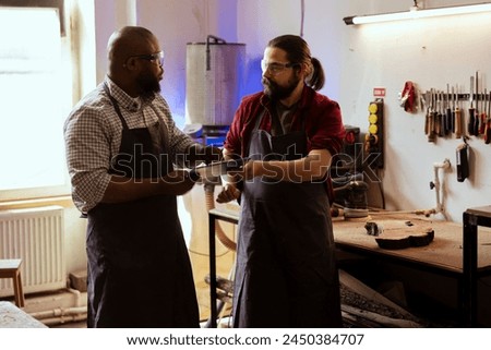 Craftsperson and colleague looking over technical schematics to make commissioned wooden object. Manufacturer and coworker looking at blueprints to execute furniture assembling woodworking project Royalty-Free Stock Photo #2450384707