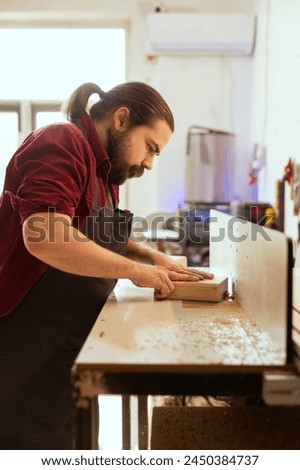 Craftsperson putting lumber block though spindle moulder, doing furniture assembling. Joiner in carpentry studio using heavy machinery to perform various manufacturing tasks, enjoying diy hobby Royalty-Free Stock Photo #2450384737