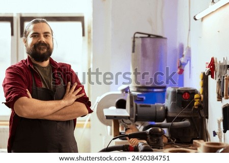 Portrait of upbeat woodworking professional preparing to start production in messy furniture assembly shop. Cheerful craftsperson in studio at workbench ready to cut wood pieces Royalty-Free Stock Photo #2450384751