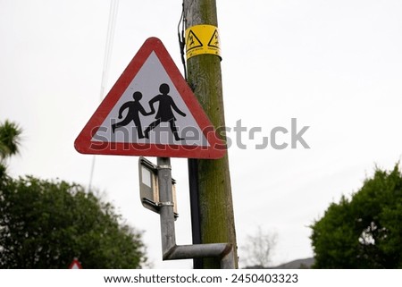 Telephone pole wooden structure Triangular pedestrian crosswalk sign metal, shows walking person female person parent gender neutral child holding hands. Yellow electrical wire warning death sign
