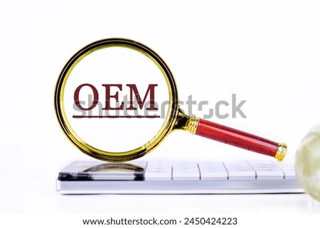 OEM original equipment manufacturer concept. Text through a magnifying glass on a calculator on a light background