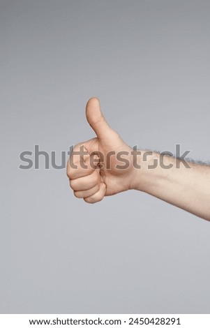 Vertical studio shot of unrecognizable mans hand showing thumb up sign, gray background, copy space