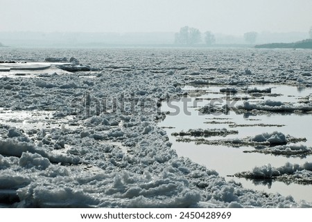 Thick ice blankets the River Elbe in Northern Germany, transforming its surface into a wintry wonderland. The frozen expanse reflects the pale sunlight, creating a serene and mesmerizing sight. Royalty-Free Stock Photo #2450428969