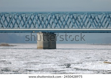 Thick ice blankets the River Elbe in Northern Germany, transforming its surface into a wintry wonderland. The frozen expanse reflects the pale sunlight, creating a serene and mesmerizing sight. Royalty-Free Stock Photo #2450428975