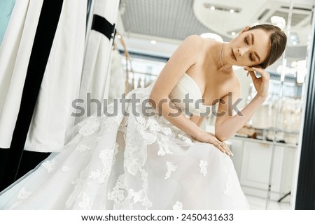 A young, beautiful brunette bride in a stunning white wedding dress gazes at her reflection in a mirror.