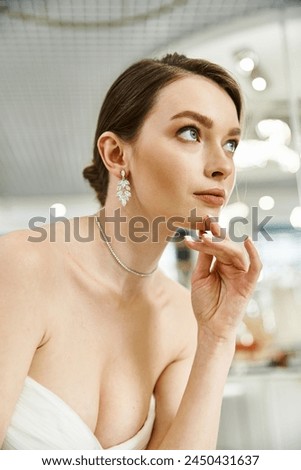 A stunning brunette bride in a strapless dress strikes a pose, exuding elegance and confidence in a wedding salon setting.