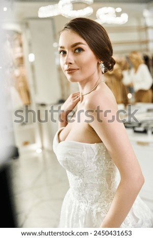 A young brunette bride in a white wedding dress strikes a pose for a picture in a wedding salon.