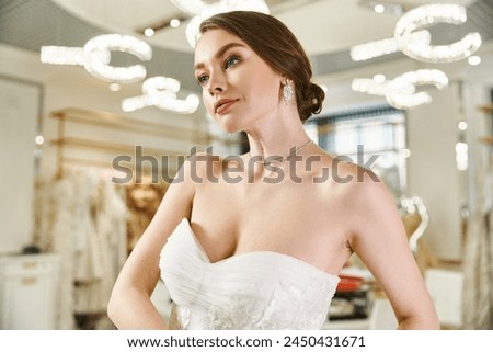 A young, beautiful bride in a white dress gazes at her reflection in a mirror in a wedding salon.