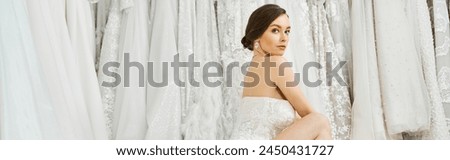 A young brunette bride poses elegantly in a white dress in a wedding salon, exuding charm and grace.