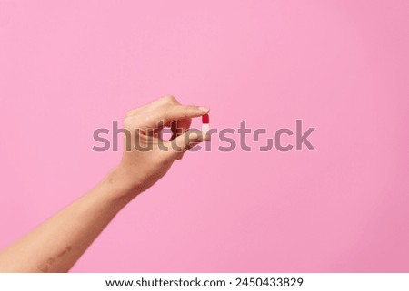  female hand delicately holds a white pill between fingers against a pink isolated background, symbolizing healthcare, dietary supplements, and treatment for conditions such as depression and diseases