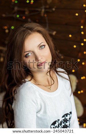 beautiful smiling girl in warm white jacket sits near the window next to the wall in the lights