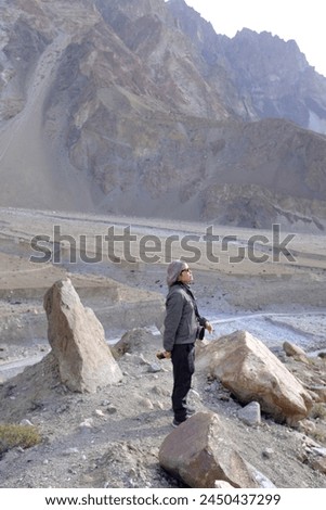 An Asian female tourist posing for a picture with the view of tall mountains in Passu Valley, Gilgit-Baltistan, Pakistan.
