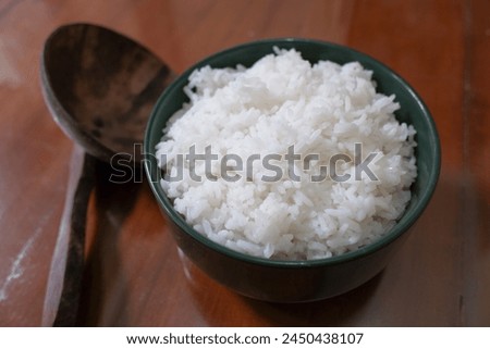 A bowl of white rice and a wooden ladle on a brown wooden table, food, stock photo.