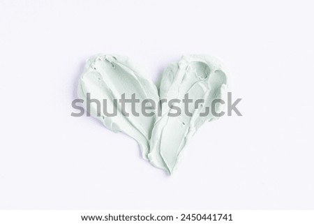 Green clay mask or correcting concealer smear smudge in the shape of a heart on white background.  Royalty-Free Stock Photo #2450441741