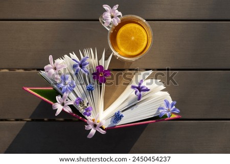book standing vertically and small spring flowers between the pages, cup of tea on table, illuminated by sun. Picture of peaceful morning. atmosphere of relaxation, tea time. Read book with pleasure