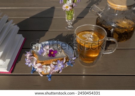 bread toast with spring flowers, a glass cup of tea and a teapot - a beautiful healthy breakfast. Pages of an open book on a table on a sunny day. good morning, floral fantasies, relaxing atmosphere