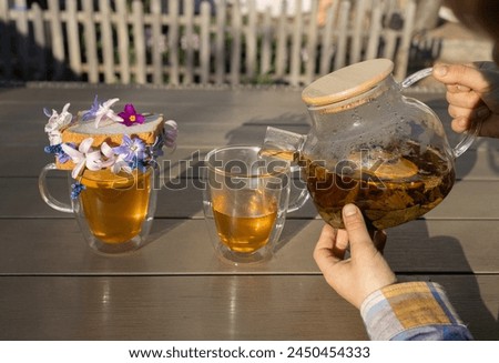 children's hands with transparent teapot from which he pours tea into two glass cups. bread toast with spring flowers. Breakfast for mom on Mother's Day. good morning, floral fantasies, relaxing
