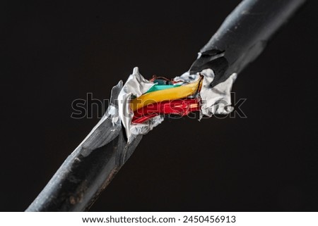 A close up of a broken electric cord with red and electric yellow wires intertwined. Damaged power electrical cable on black background
