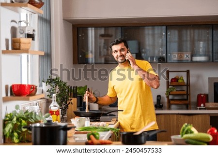 Indian young handsome man in kitchen taking selfie picture while cooking, using tablet pc and having coffee