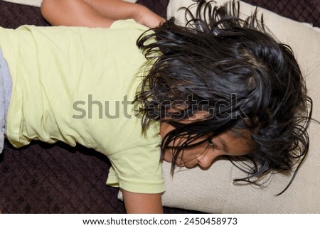 A photo of a peaceful young girl curled up on a cozy sofa, gently twirling strands of her own hair.