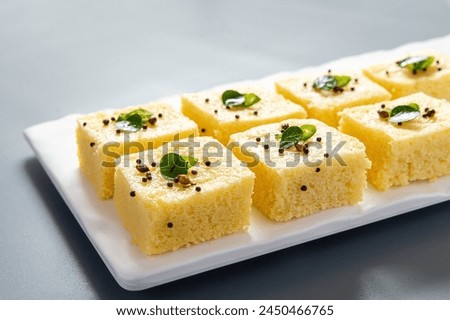 Yellow dhokla plated in a white plate on a grey background with negative space to write copy.