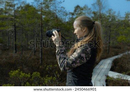 A woman with a camera takes pictures of pines in a natural swamp