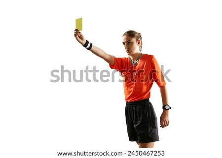 Serious and concentrated young woman, soccer referee controlling game, showing yellow card as waning symbol against white background. Concept of sport, competition, match, profession, football game