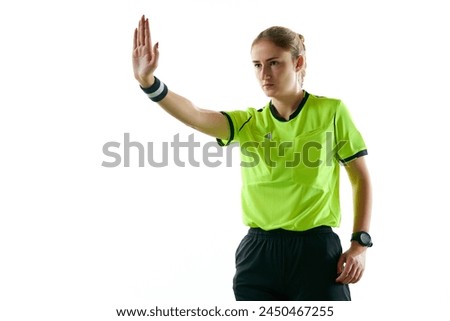 Young serious woman, soccer referee gesturing, raising hand forward meaning penalty kick against white studio background. Concept of sport, competition, match, profession, football game, control