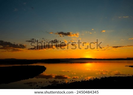 Sunset background photo. Sunrays and partly cloudy sky over the lake with reflections.