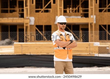 roofer builder working on roog structure of building on construction site. handsome young male builder in hard hat smiling at camera. Construction Worker on Duty. Contractor and the Wooden House Frame Royalty-Free Stock Photo #2450498629