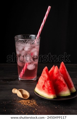 Close-up of plate with pieces of watermelon with brown sugar and glass of juice with ice, black background, vertical, with copy space