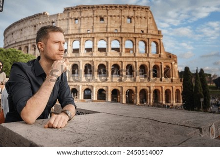 Man in dark shirt leaning on stone ledge at Colosseum, Rome, Italy. Contemplative pose with iconic amphitheater in background. Leisure and reflection theme.